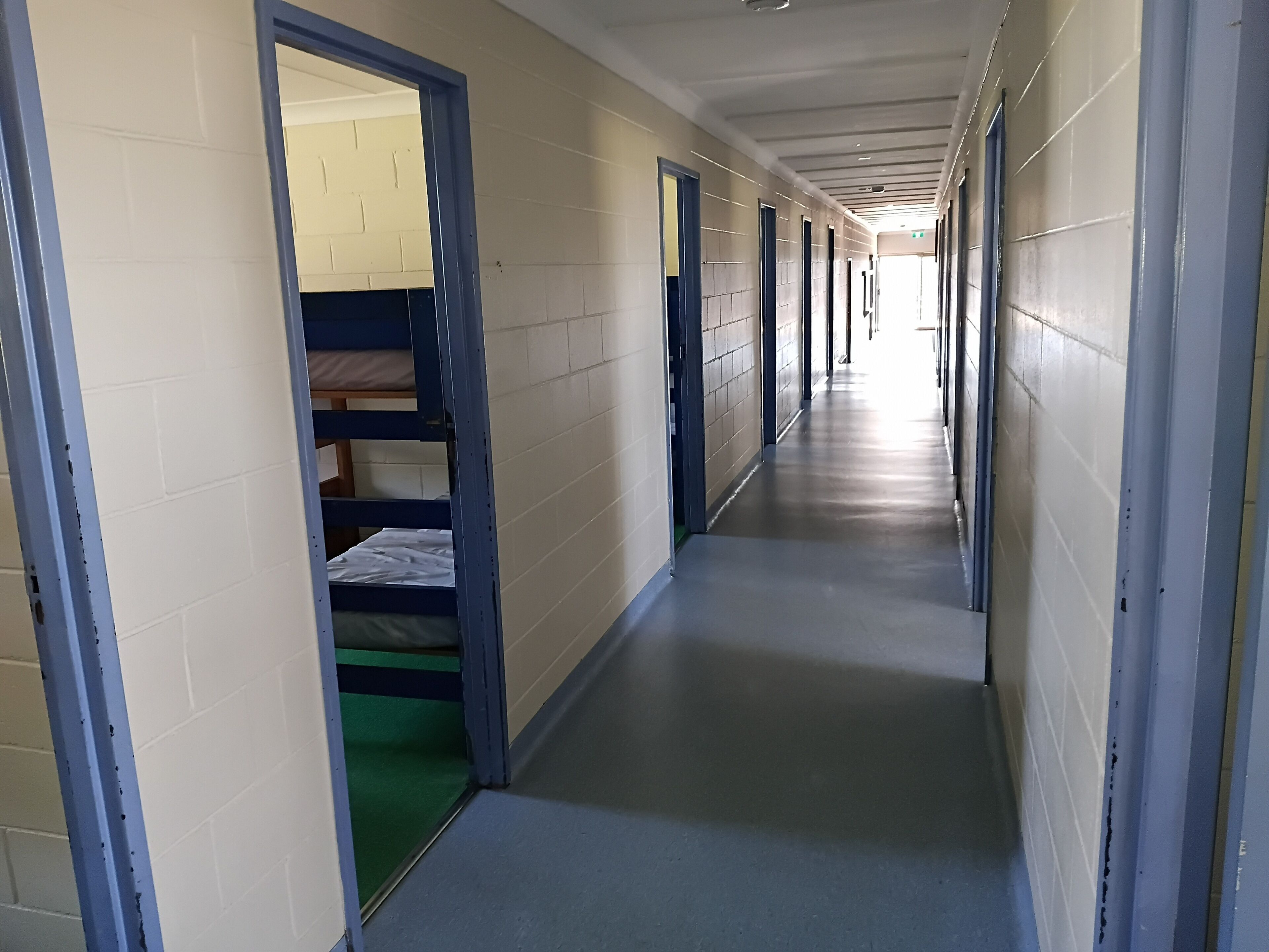 A corridor with bunk beds on the left, a tiled wall, and doors leading to individual rooms.