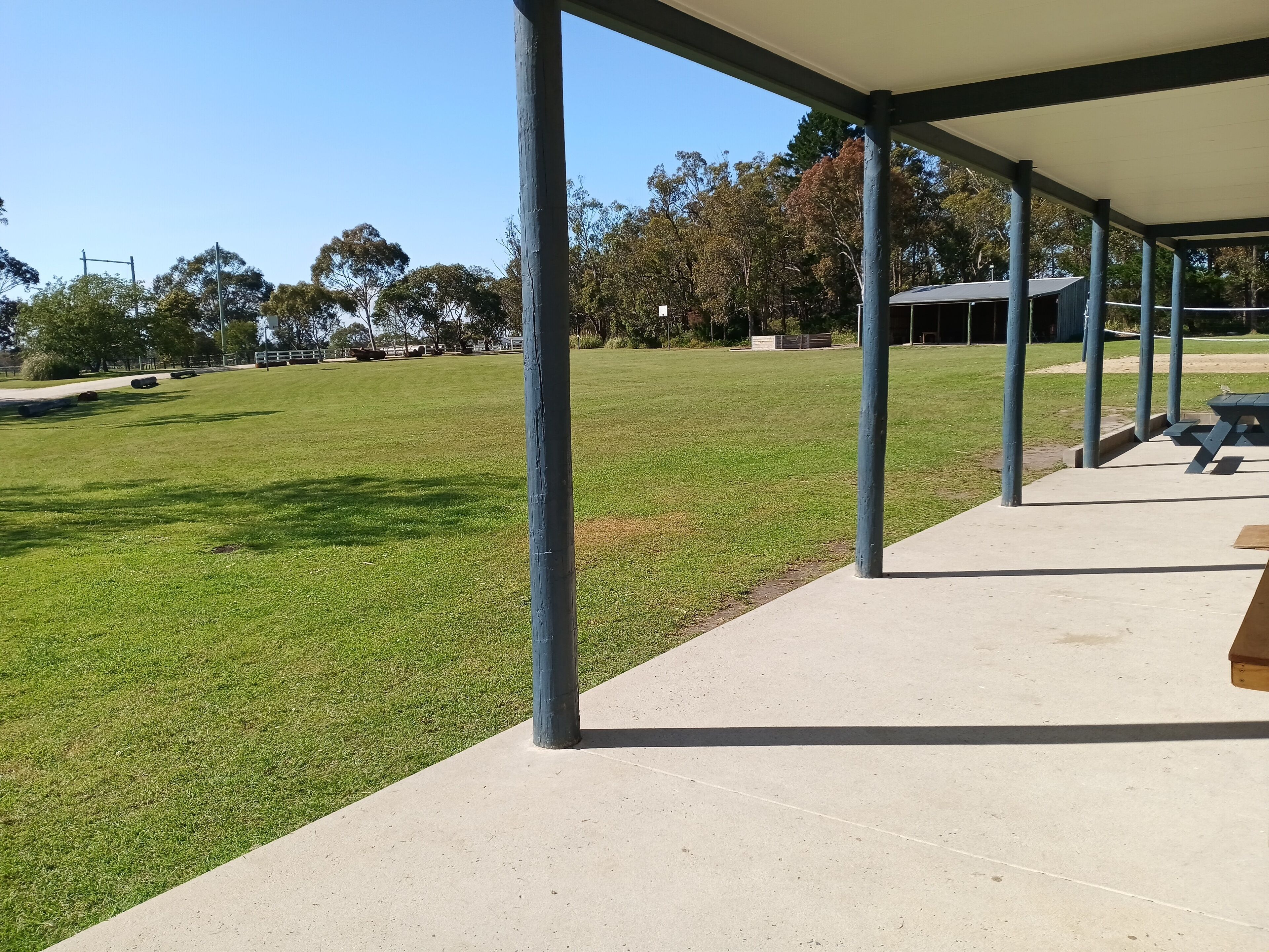 A covered outdoor area with a picnic table and a grassy field.