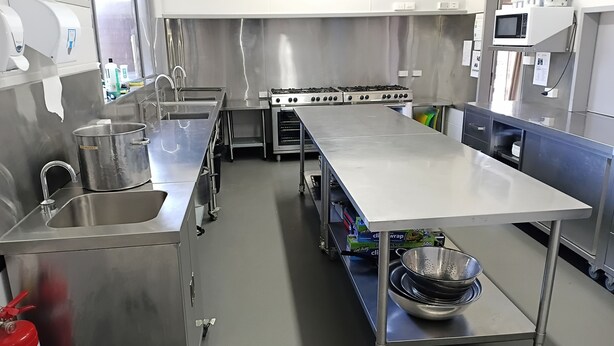 Et kommercielt stålkøkken med stor arbejdsflade, vask, brandslukker og mikrobølgeovn.
