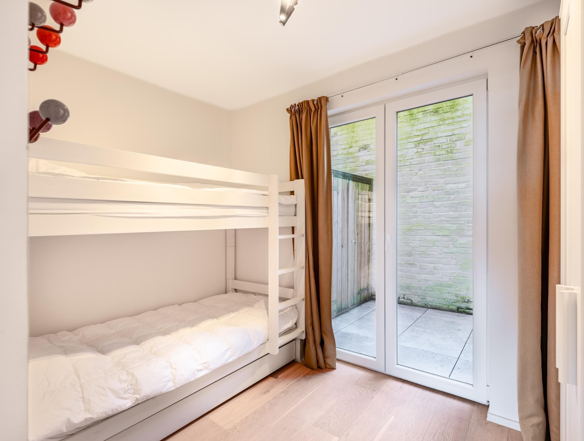 Une chambre avec un lit superposé, une porte-fenêtre coulissante donnant sur un balcon et une petite étagère avec des lunettes de soleil.