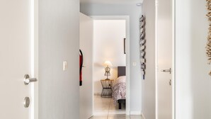 A hallway leading to a bedroom with a bed, a bedside table, and a lamp. There is a door on the left and a wall with a sign on the right. - Modernly furnished flat in St-Idesbald (Sint-Idesbald)