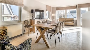 A modern living room with a dining area, large windows, and a flat-screen TV. - Modernly furnished flat in St-Idesbald (Sint-Idesbald)