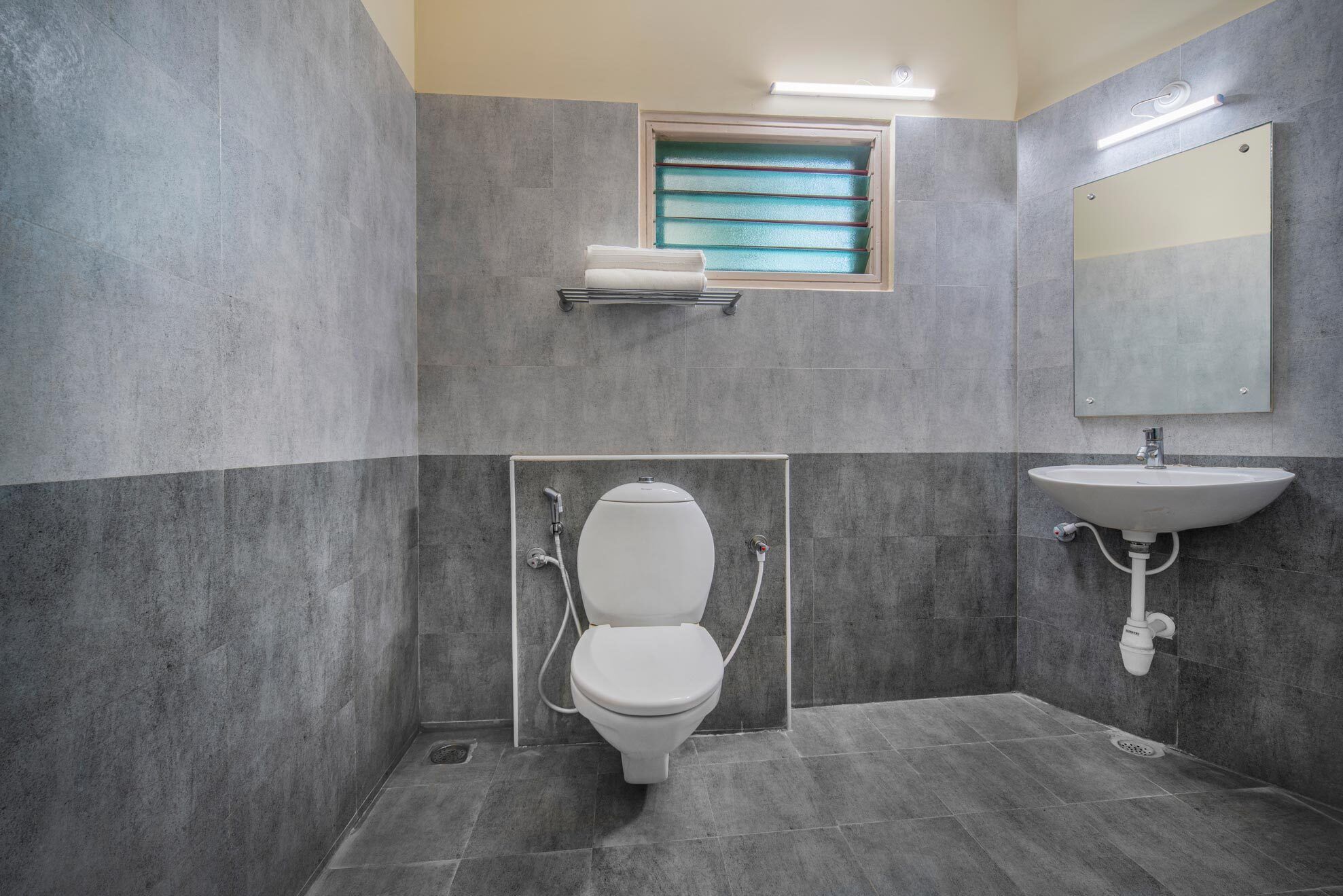 Un baño moderno con inodoro, lavamanos y ventana con toallero.