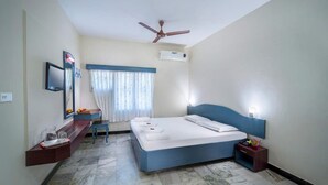 Habitación de hotel con cama, escritorio, silla, ventilador de techo y ventana con cortinas.