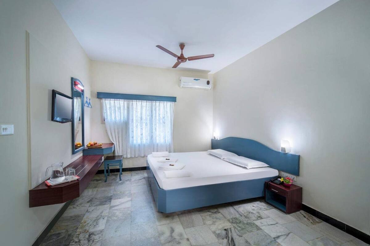 A hotel room with a bed, a desk, a chair, a ceiling fan, and a window with curtains.