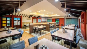 Un restaurante moderno con techos altos, vigas a la vista y una combinación de paredes de madera y ladrillo. Las mesas están dispuestas en forma de U, y hay varias cabinas.