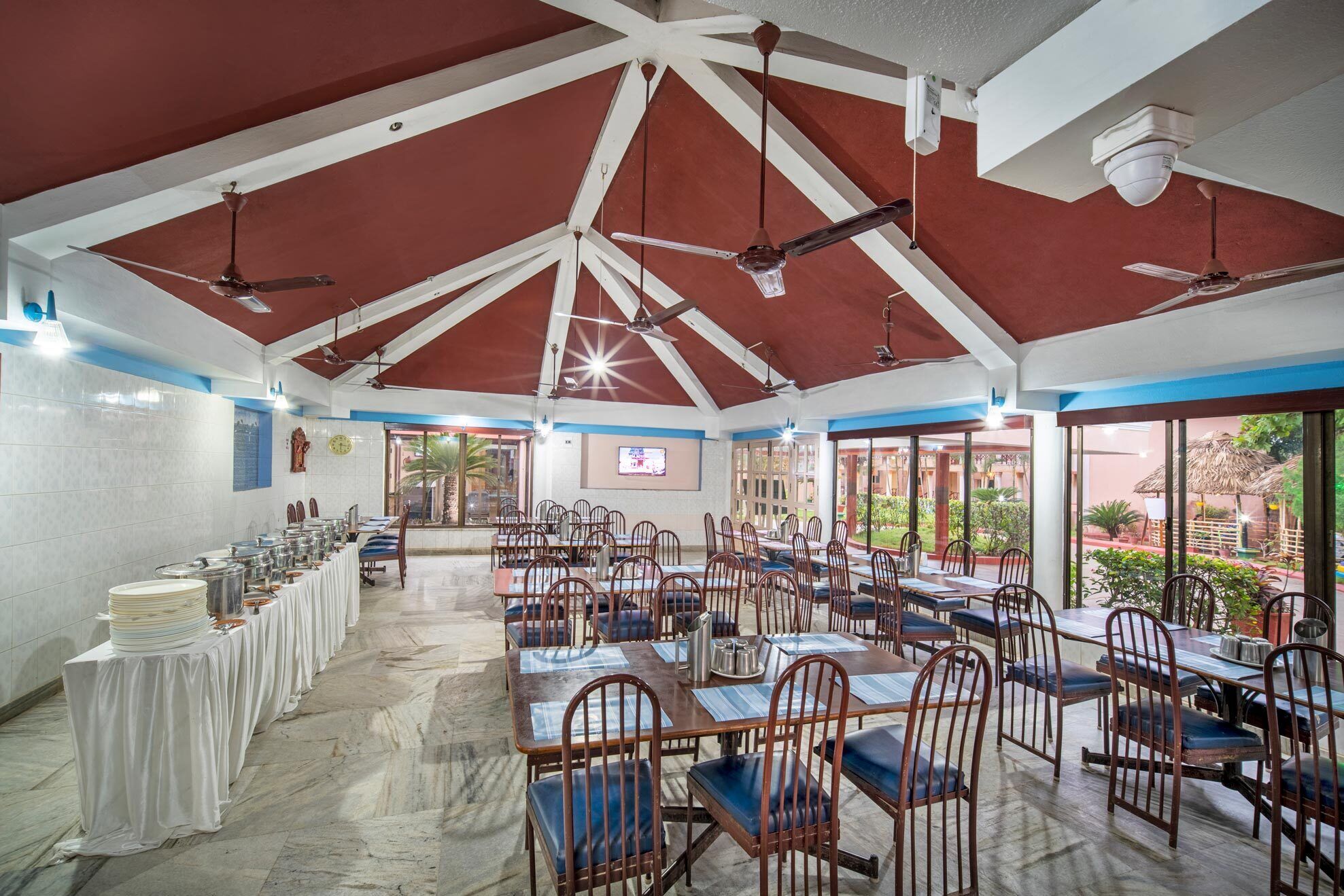 A spacious indoor dining area with high ceilings, multiple tables and chairs, and a view of the outdoors.
