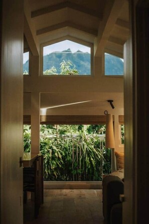 Una stanza con soffitto alto, vista sul verde e una lampada.