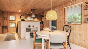 Et træindrettet rum med et spisebord, stole, en hængende lampe og et køkken med komfur og skabe.