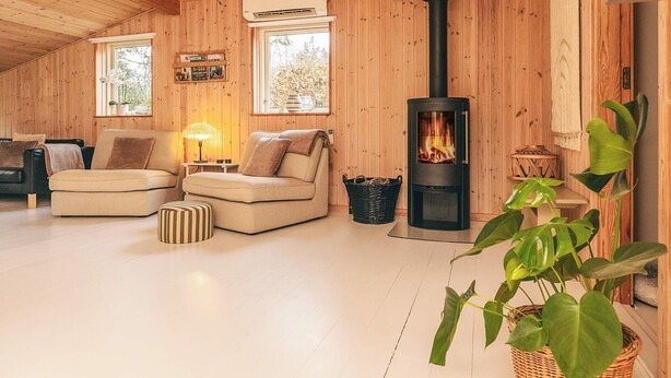 En hyggelig hyttekrog med træbeklædt loft, en sort brændeovn, to sofaer, en lampe og en potteplante.