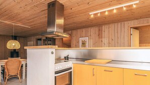 Et moderne køkken med træpaneler, et rustfrit stål emfang, en indbygget ovn og en stor køkkenø med skærebræt.