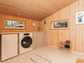 Une petite cuisine aux murs en bois, avec un lave-linge, un évier et une étagère où sont rangées des chaussures.