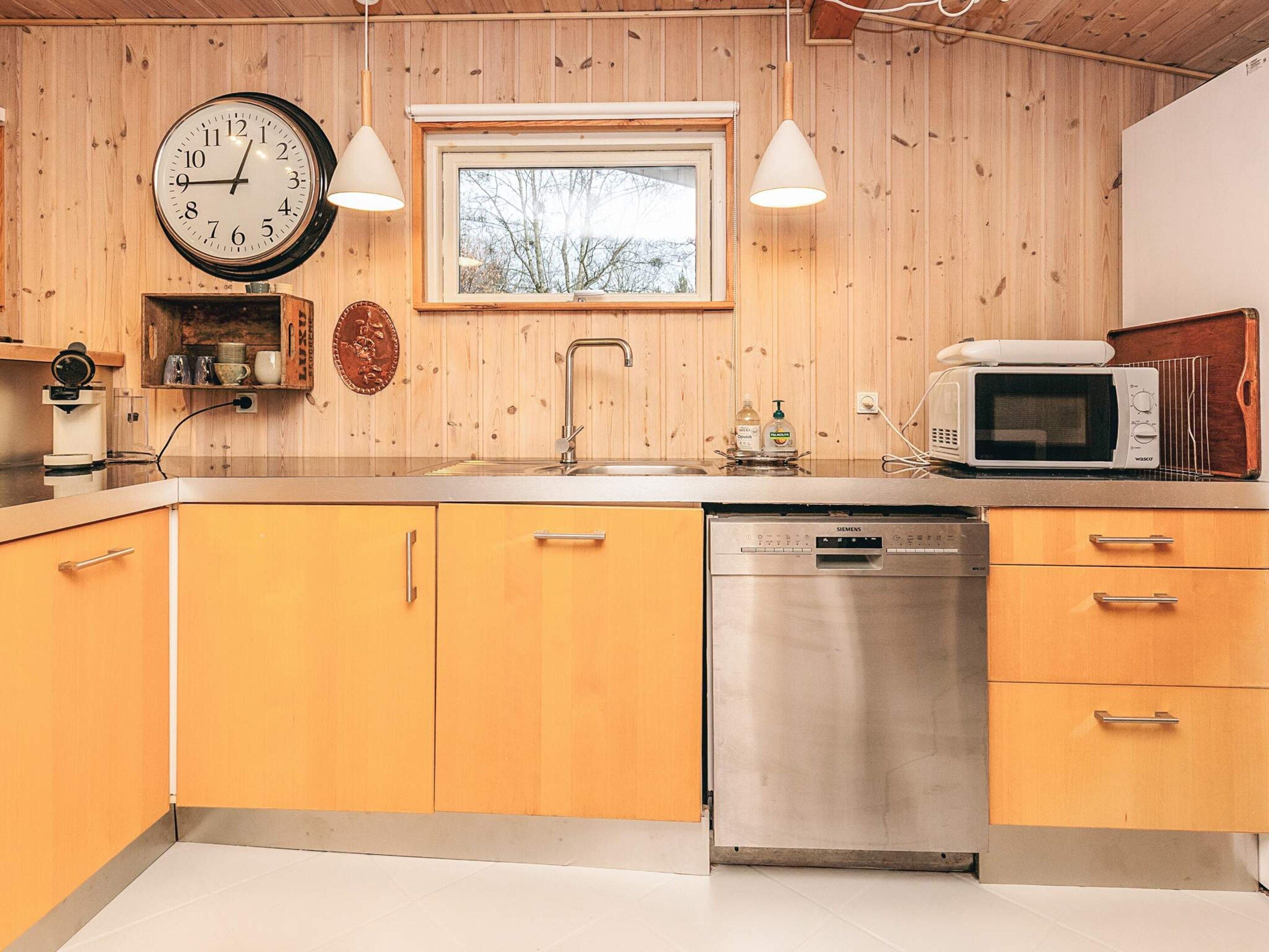 Une cuisine avec des meubles en bois, un lave-vaisselle en acier inoxydable, un four à micro-ondes, un évier et une horloge murale.