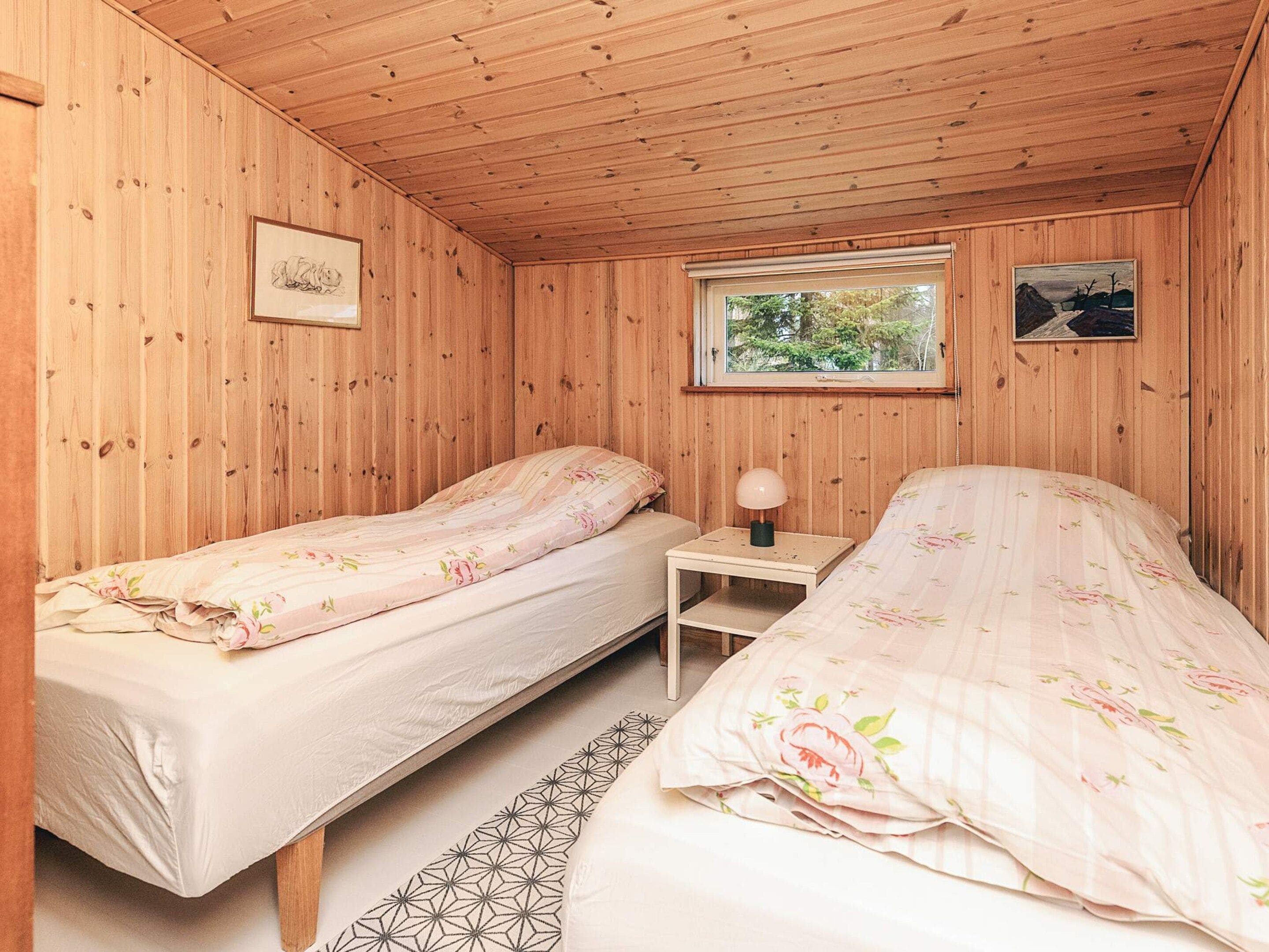 A cabin with two beds, a window with a view of trees, and a small table with a lamp.