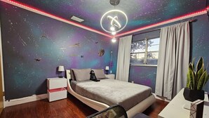 Ein Schlafzimmer mit Bett, Nachttischen, einem Schreibtisch, einem Stuhl, einem Fenster und einer Deckenleuchte.