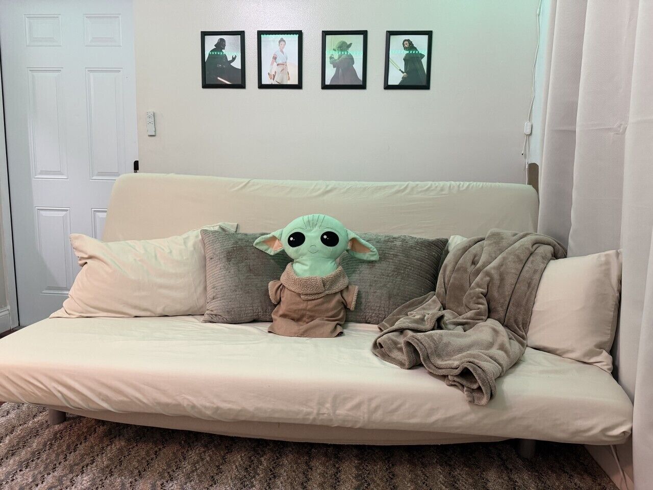 A beige sofa with a plush toy in the center, a blanket draped over it, and framed pictures on the wall.