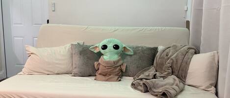 A beige sofa with a plush toy in the center, a blanket draped over it, and framed pictures on the wall.