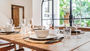Een eettafel gedekt met witte kommen, borden, bestek en glazen, met uitzicht op groen door een groot raam.