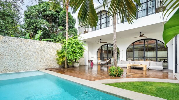 Een modern huis met een zwembad, een houten terras en een zitgedeelte buiten.