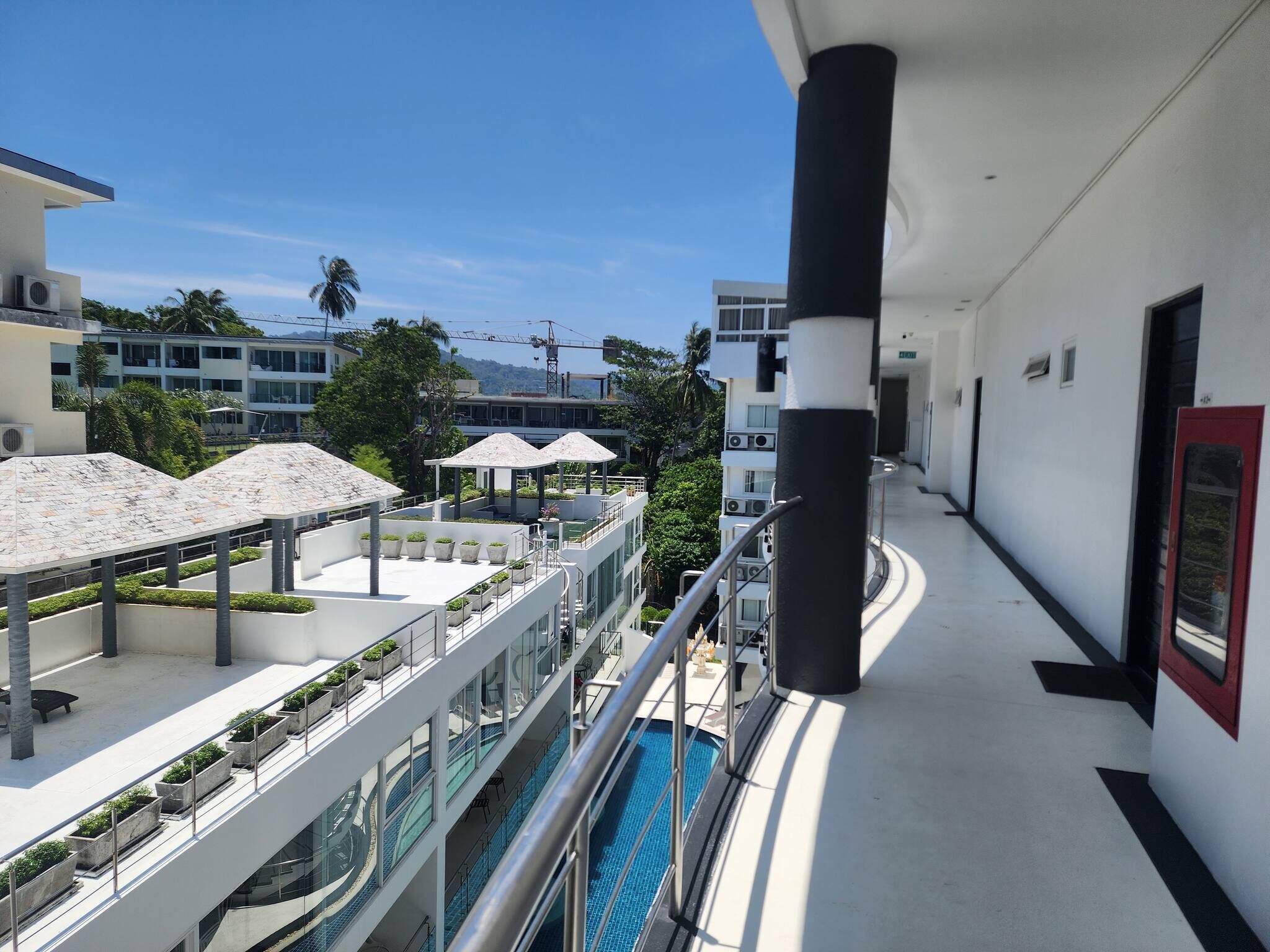 En modern hotellkorridor med en pool, utomhusmöbler och utsikt över andra byggnader.