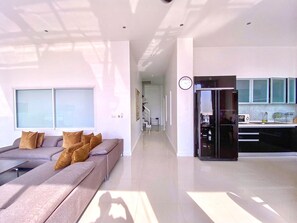 A modern living room with a sofa, a kitchen area with a refrigerator, and a hallway. - A2 - 4 Bedrooms Duplex Serviced Apartment with Stunning Sea View, Karon Beach (Tambon Karon)