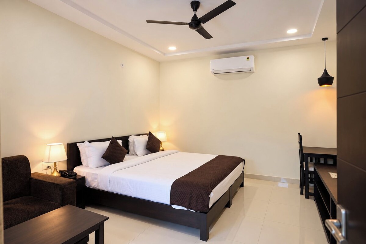 Habitación de hotel con cama, mesitas de noche, escritorio, silla, ventilador de techo y aire acondicionado.