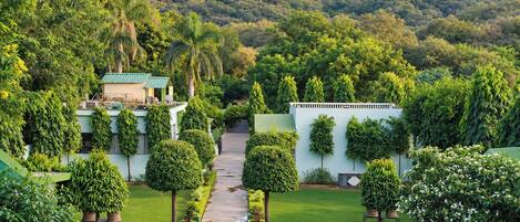 A well-maintained garden with a pathway leading to a building, surrounded by lush greenery and hills in the background.