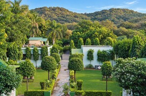 A well-maintained garden with a pathway leading to a building, surrounded by lush greenery and hills in the background.