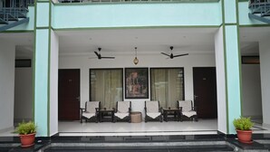 A building entrance with a covered porch, two potted plants, a seating area with chairs, and a staircase leading to the entrance. - Ranthambhore Vatika Resort (Sawai Madhopur)
