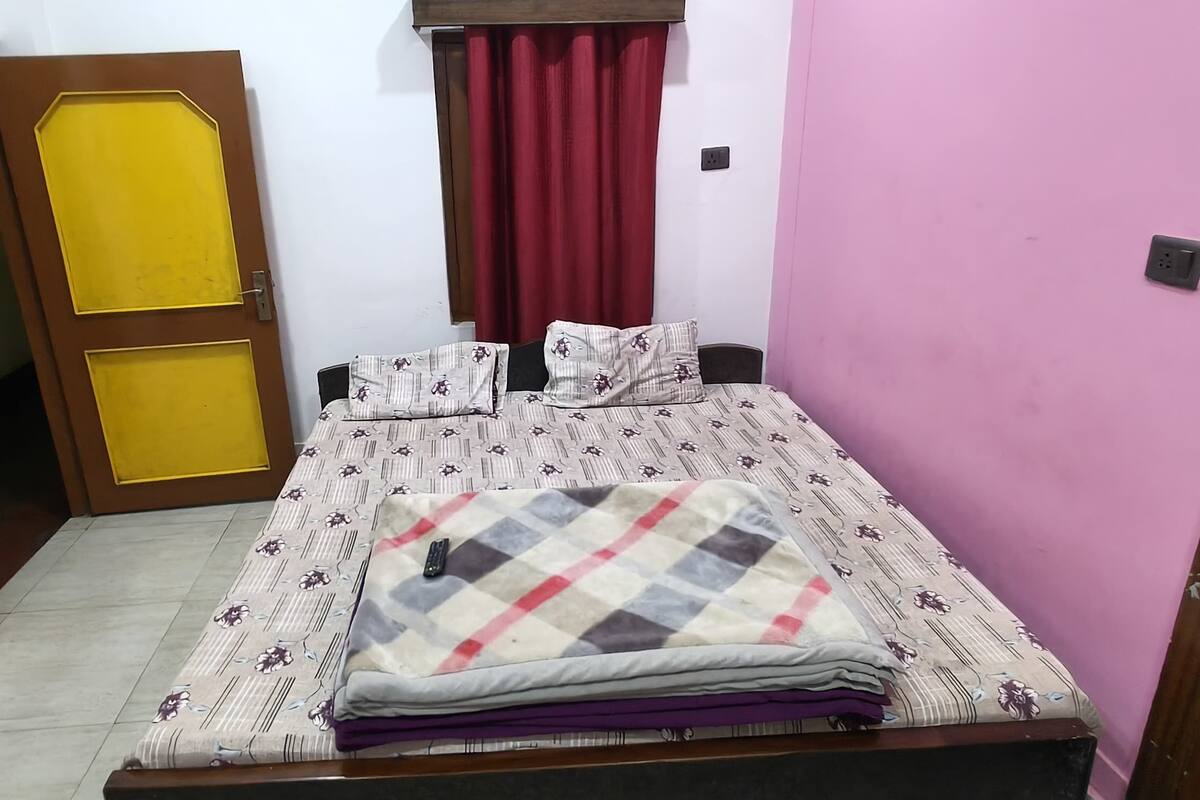 A small bedroom with a bed, a bedside table, a chair, a door, and a wall socket.