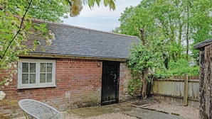 A brick building with a tiled roof, a black door, and a small patio area with a wicker chair and a round table. - 1 bedroom accommodation in Sturminster Newton (Sturminster Newton)