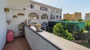 Ein Balkon mit Blick auf ein Gebäude mit Rundbogenfenstern, einer grünen Plane und Blumentöpfen.