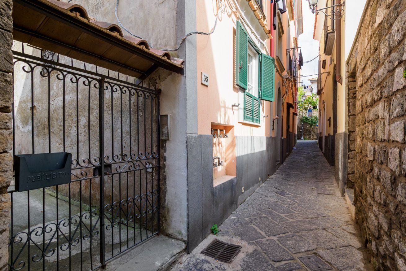 A narrow cobblestone street flanked by buildings with traditional architecture, a metal gate, and a mailbox.