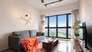 A modern living room with a grey sofa, a coffee table, a TV, and a large window offering a city view. - KLCC Agile Bukit Bintang---5 mins to TRX (Kuala Lumpur)