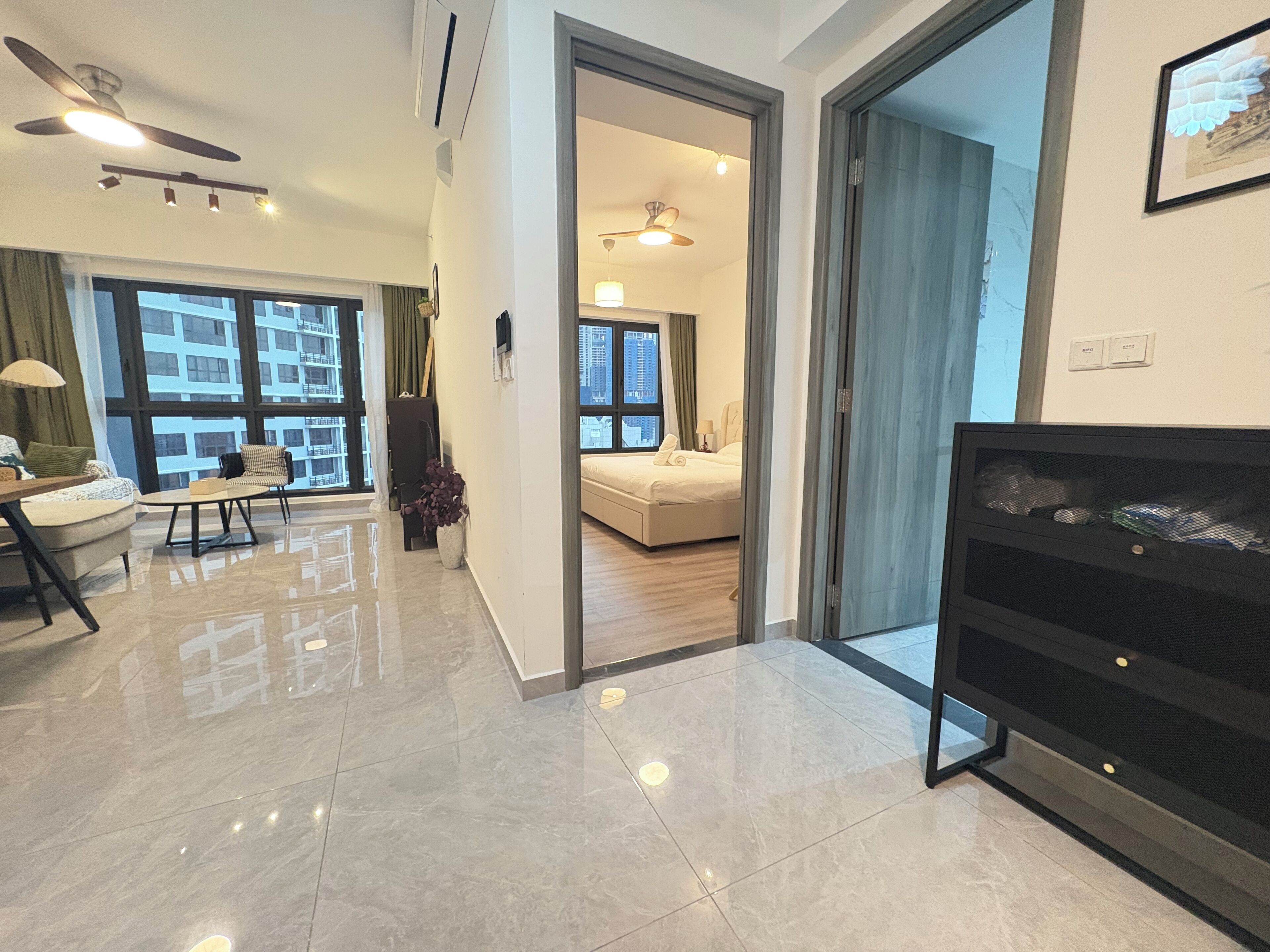 A modern hotel room with a large bed, a seating area with a sofa and armchairs, a dining table, and a view of the cityscape through large windows.