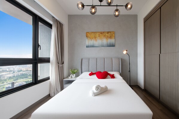 Ein modernes Hotelzimmer mit einem großen Bett, Blick auf die Stadt, einem Bild an der Wand und einem roten Kissen.