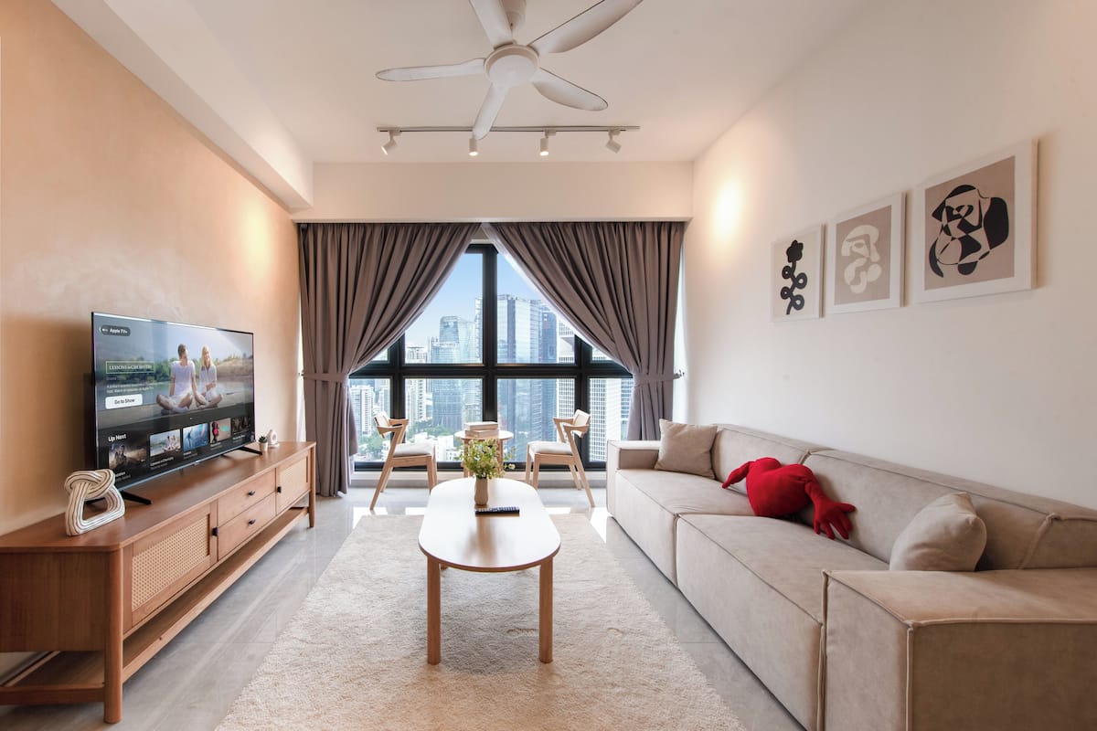 A modern living room with a flat-screen TV, a ceiling fan, a sofa, and a large window with a city view.