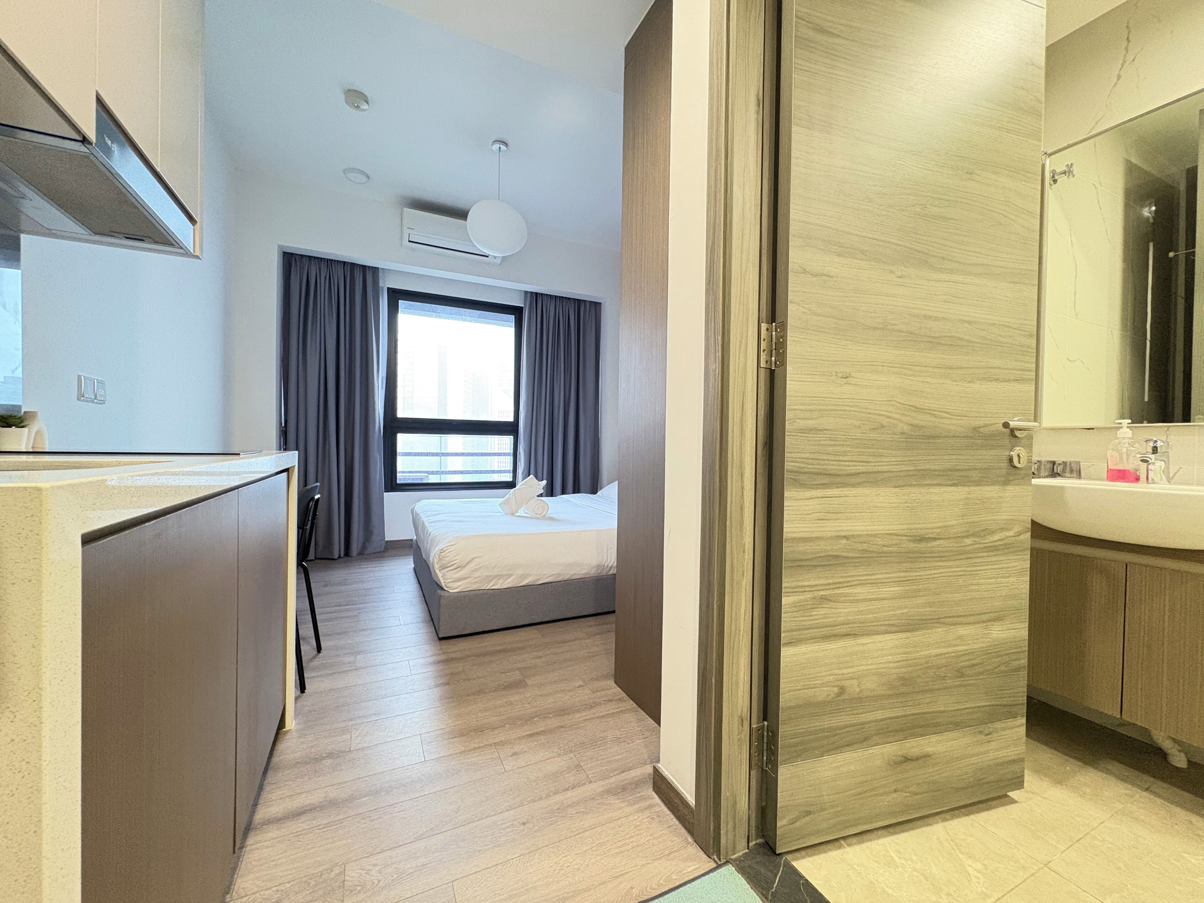 A modern hotel room with a bed, a desk, a bathroom with a mirror, and a window with curtains.
