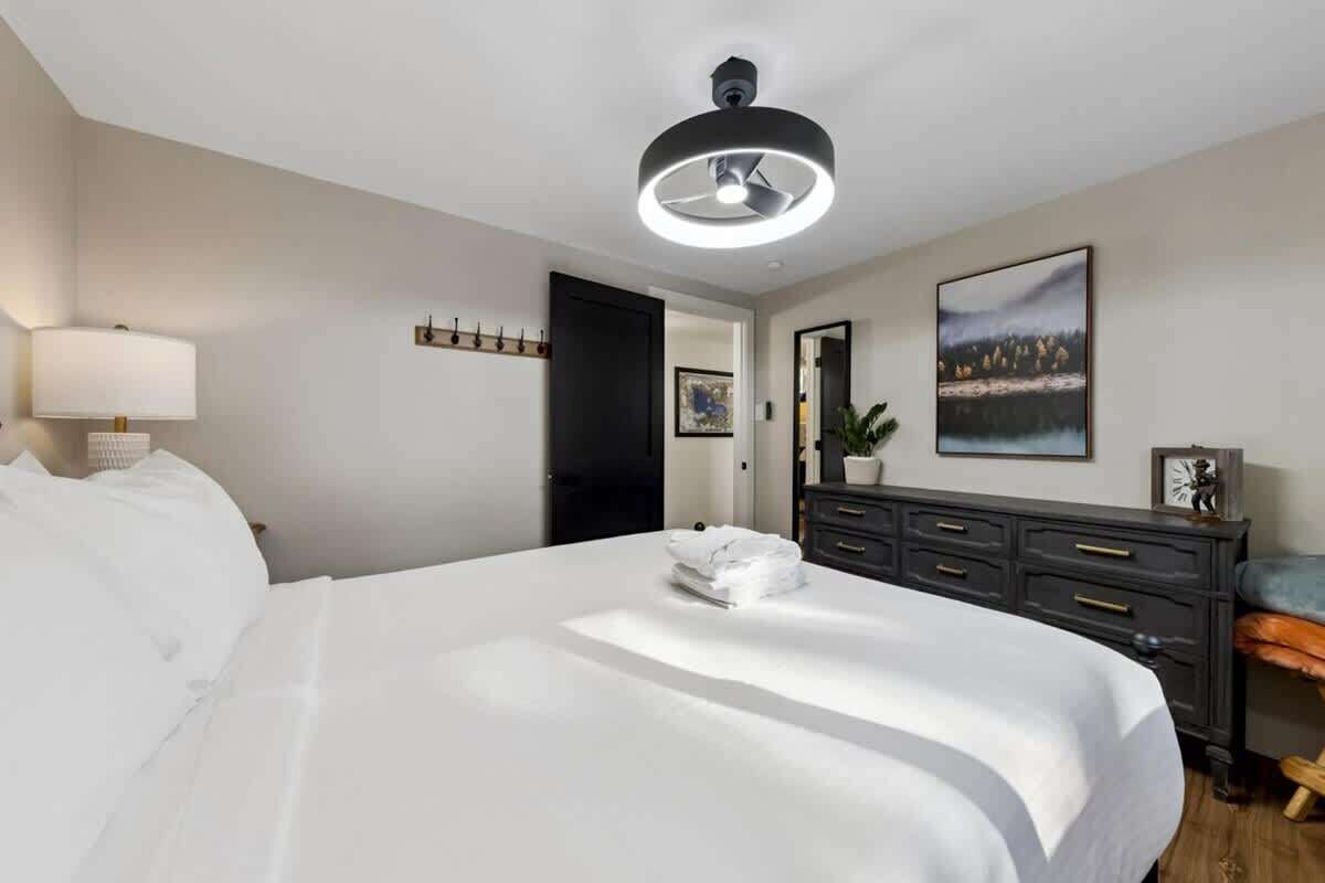 Ein Hotelzimmer mit einem großen Bett, einer Nachttischlampe, einem Deckenventilator, einem Schminktisch und einem gerahmten Bild an der Wand.