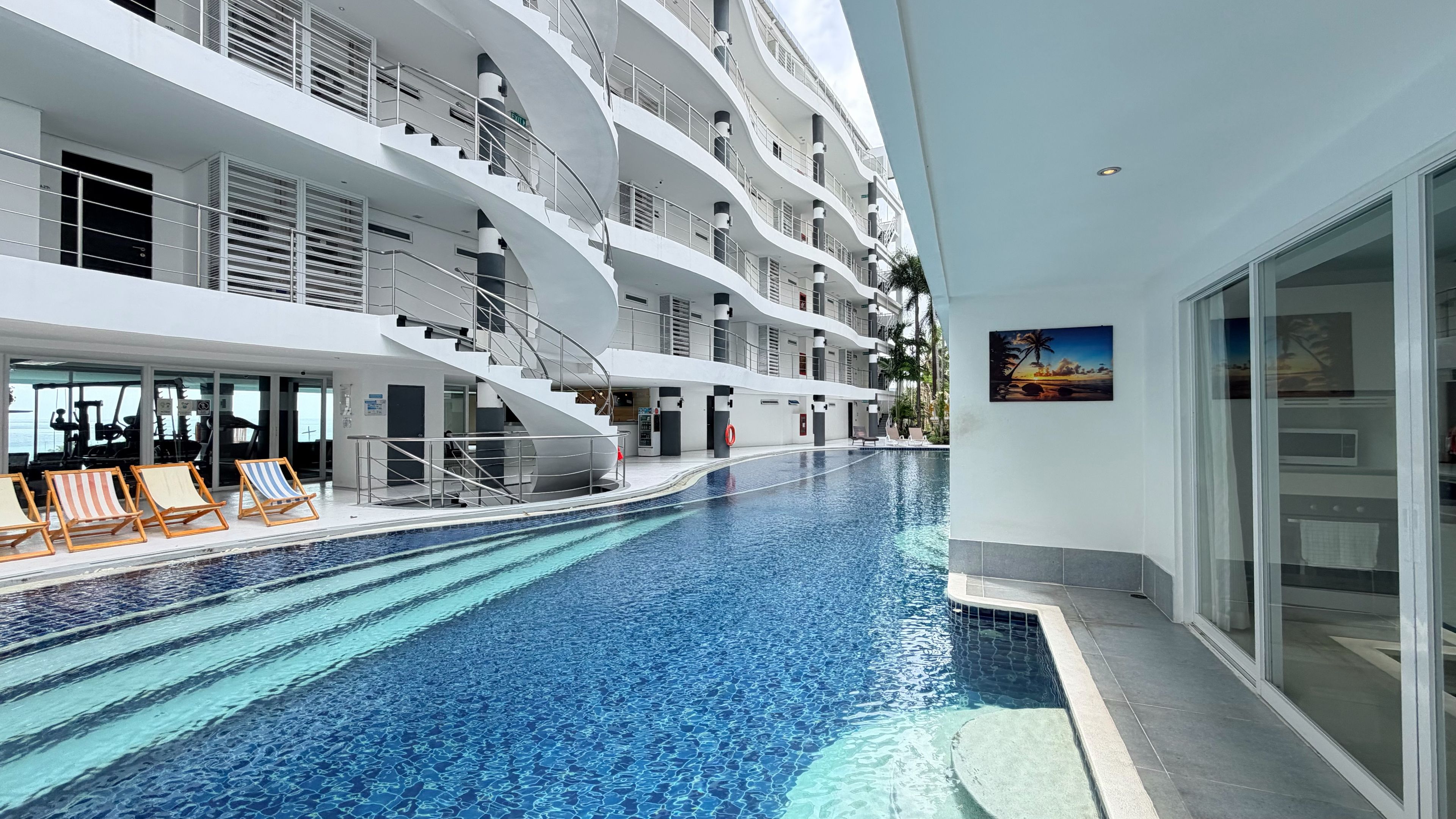 A modern hotel interior with a swimming pool, multiple balconies, and a view of the sea.