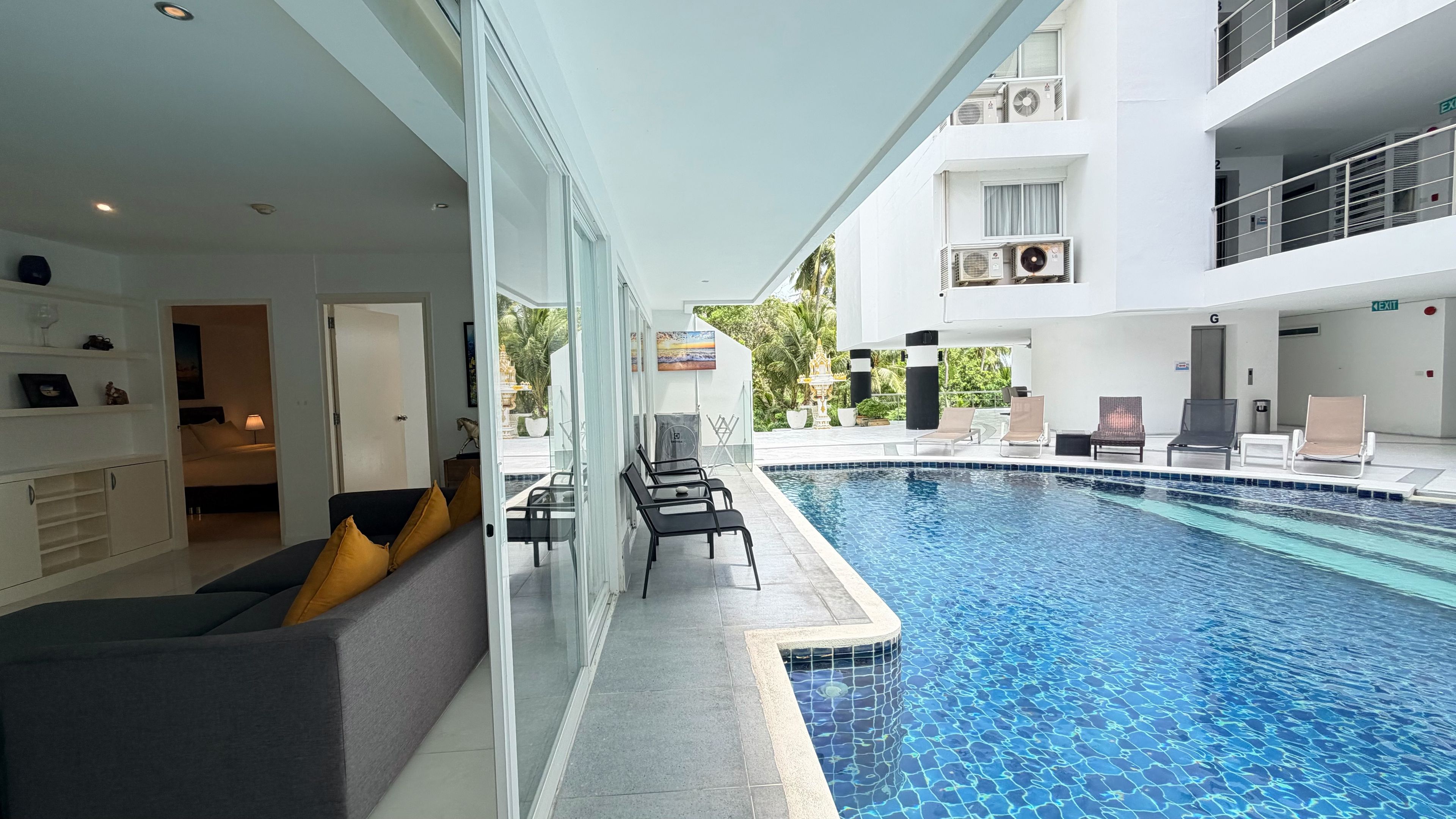 Una moderna camera d'albergo con piscina, divano con cuscini, zona pranzo e balcone con poltrone reclinabili.