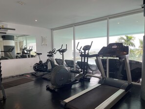 Ein modernes Fitnessstudio mit Trainingsgeräten, großen Fenstern und Blick auf Palmen.
