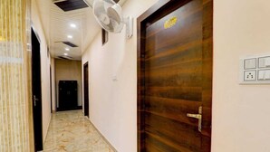 A hallway with a marble floor, a wooden door with a brass handle, and a wall-mounted fan. - Madhav Inn Lucknow (Lucknow)