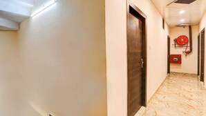 A hallway with a marble floor, a wooden door, and a red fire hose reel on the wall. - Madhav Inn Lucknow (Lucknow)