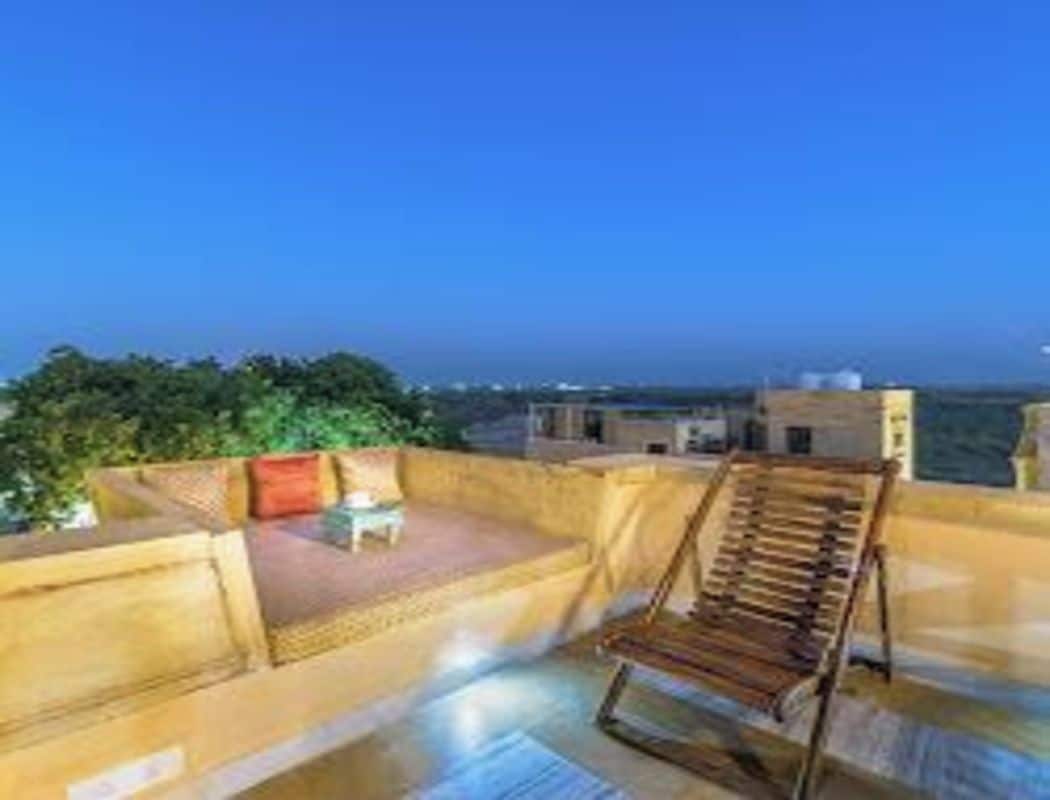 Terraza en la azotea con una silla de madera y una mesa pequeña, rodeada por un muro bajo.