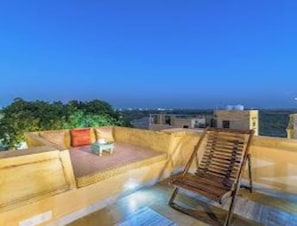 A rooftop terrace with a wooden chair and a small table, surrounded by a low wall. - Hotel Jasmin Haveli (Jaisalmer)