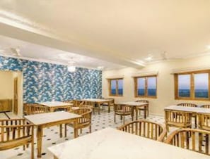 A room with multiple wooden tables and chairs, a patterned wall, and windows with a view. - Hotel Jasmin Haveli (Jaisalmer)