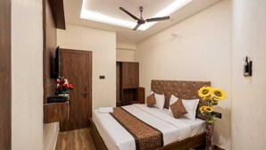 Un dormitorio con cama, ventilador de techo, armario de madera y una mesita con un florero.