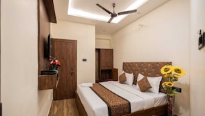 Una habitación de hotel con una cama, un ventilador de techo, un televisor montado en la pared y un armario de madera.