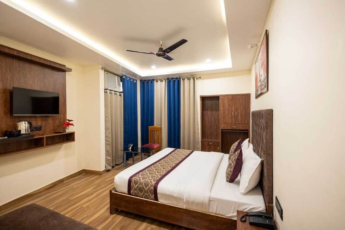 A bedroom with a bed, a TV mounted on the wall, a ceiling fan, and a wooden wardrobe.